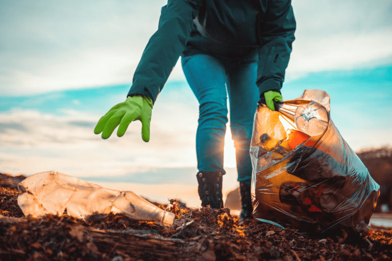 Person in green gloves collecting litter from the ground and placing it into a bag. The image highlights community cleanup efforts for environmental awareness.