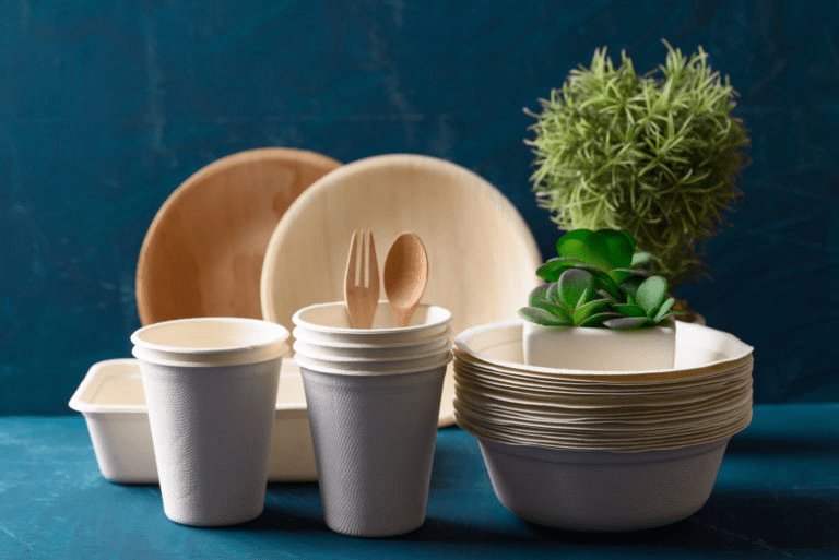 Eco-friendly disposable tableware, including cups, plates, and utensils, arranged with potted plants against a blue background.
