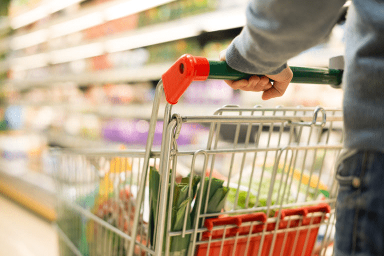 Person holding a grocery cart filled with fresh produce, shopping in a well-stocked supermarket aisle. Emphasizes a healthy lifestyle.