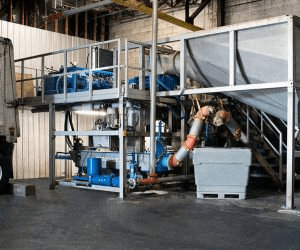Industrial machinery setup featuring a multi-level system with blue equipment and piping, used for processing materials in a factory setting.