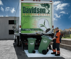 A waste management worker pulls green recycling bins from a Davidson Environmental truck, promoting eco-friendly waste solutions.
