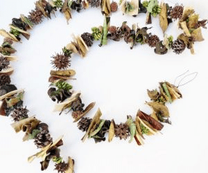 A decorative garland made from various natural materials, including leaves, pinecones, and seeds, arranged in a spiral on a white background.