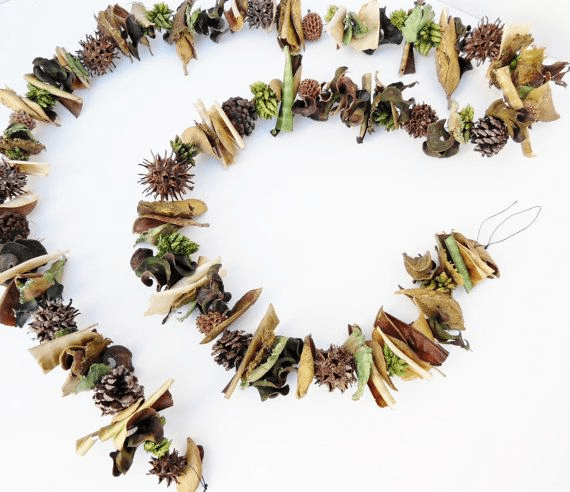 A decorative garland made of natural materials like dried leaves, pinecones, and pods, arranged in a spiral pattern. Ideal for earthy home decor.
