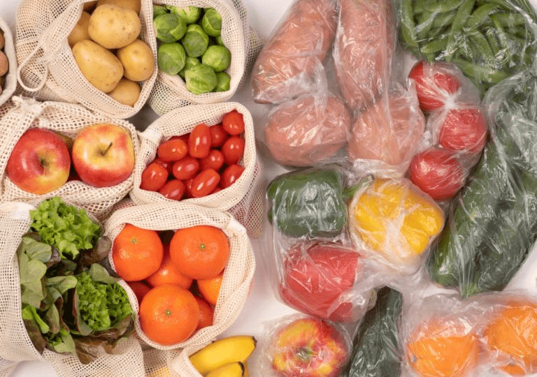 Fresh fruits and vegetables are displayed in reusable bags and plastic wrap, showcasing a variety of produce for healthy meal preparation.
