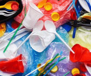 Colorful plastic waste including cups, lids, and utensils scattered on a surface, highlighting the issue of environmental pollution.